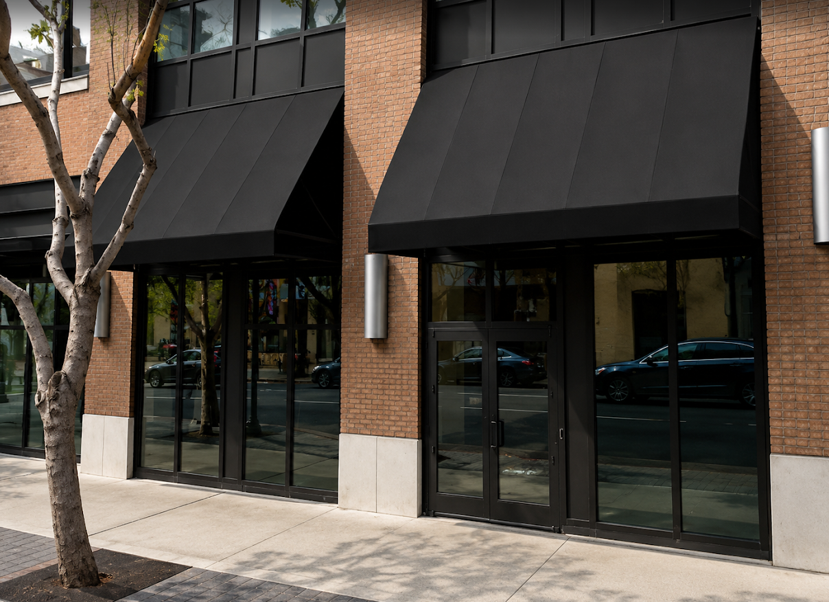 Two black shed-style awnings over glass storefront entrances on a brick building